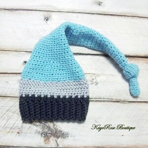 May include: A blue, gray, and black crocheted gnome hat with a long tail. The hat has a light blue top, a gray band, and a dark gray brim.