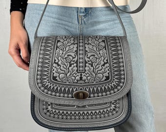 May include: A gray leather crossbody bag with a black floral design and a silver clasp. The bag has a long adjustable strap.