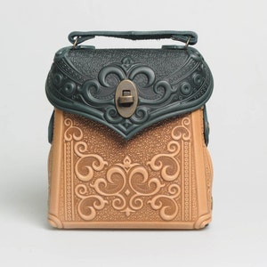 Könnte beinhalten: Eine kleine braune Ledertasche mit aufwendigen, geprägten Blumenmustern. Die obere Klappe ist aus grünem Leder mit einem dekorativen Metallverschluss.