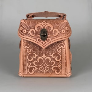 Könnte beinhalten: Eine hellbraune Lederhandtasche mit aufwendigen geprägten Schnörkeln und einem kleinen Griff. Die Tasche hat einen dekorativen Verschluss und ein strukturiertes Design, geeignet für kleine Gegenstände.