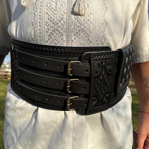 May include: A black leather belt with intricate embossed designs and multiple adjustable straps secured with brass buckles.