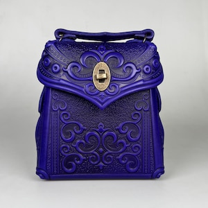 May include: A small, blue leather handbag with intricate embossed floral designs and a brass clasp. The bag has a short shoulder strap.