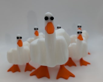 May include: Five white toy geese with orange feet and black eyes. The geese are arranged in a semi-circle with the front goose facing the camera.