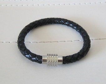 May include: A black leather bracelet with a silver magnetic clasp. The bracelet is braided and has a simple design.