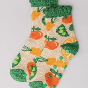 May include: A pair of beige socks with a repeating pattern of orange tomatoes, carrots, and green peas. The cuffs and toes are green, and the soles have green non-slip dots. These cozy socks are perfect for adding a touch of fun to any outfit.