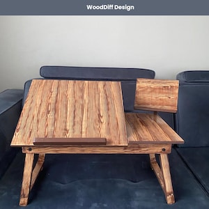 May include: A wooden laptop stand with a built-in phone holder. The stand has a brown wood grain finish and is foldable. WoodDiff Design is printed on the top of the stand.