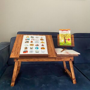May include: A wooden laptop stand with a book and a piece of paper on it. The stand is on a blue sofa. The book is titled "ÇOCUK KALBİ".