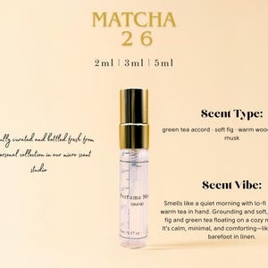May include: A small glass bottle of perfume with a gold cap and a label that says "Perfume No. Brand". The bottle is sitting on a light brown surface. The text "MATCHA 26" is at the top of the image. The text "2ml | 3ml | 5ml" is below the text "MATCHA 26". The text "Scent Type: green tea accord - soft fig - warm woods - skin-like musk" is on the right side of the image. The text "Scent Vibe: Smells like a quiet morning with lo-fi playing and warm tea in hand. Grounding and soft, with creamy fig and green tea floating on a cozy musky base. It's calm, minimal, and comforting-like journaling barefoot in linen." is also on the right side of the image.