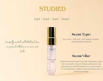 May include: A clear perfume vial with a gold cap, labeled with measurements from 2ml to 10ml. The text reads "STUDIED" and describes the scent type as airy musk, soft orris, pink pepper sparkle, and cedarwood skin warmth. The scent vibe is described as introspective, modern, and minimalist.