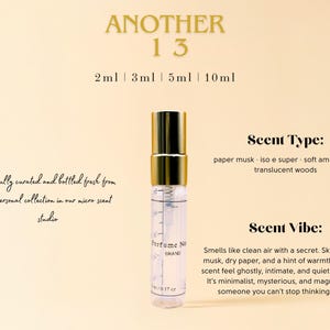 May include: A small, clear glass bottle with a gold cap and a white label that says "Perfume No. 13 BRAND". The bottle is sitting on a light beige background. The text "ANOTHER 13" is at the top of the image. The text "2ml 3ml 5ml 10ml" is below the text "ANOTHER 13". The text "Scent Type: paper musk iso e super soft ambergris translucent woods" is on the right side of the image. The text "Scent Vibe: Smells like clean air with a secret. Skin-hugging musk, dry paper, and a hint of warmth make this scent feel ghostly, intimate, and quietly addictive. It's minimalist, mysterious, and magnetic-like someone you can't stop thinking about." is also on the right side of the image.