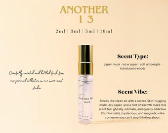 May include: A small, clear glass bottle with a gold cap and a white label that says "Perfume No. 13 BRAND". The bottle is sitting on a light beige background. The text "ANOTHER 13" is at the top of the image. The text "2ml 3ml 5ml 10ml" is below the text "ANOTHER 13". The text "Scent Type: paper musk iso e super soft ambergris translucent woods" is on the right side of the image. The text "Scent Vibe: Smells like clean air with a secret. Skin-hugging musk, dry paper, and a hint of warmth make this scent feel ghostly, intimate, and quietly addictive. It's minimalist, mysterious, and magnetic-like someone you can't stop thinking about." is also on the right side of the image.