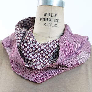 May include: A purple and white patterned scarf with a floral design. The scarf is folded and displayed on a mannequin.