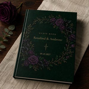 Könnte beinhalten: Ein dunkelgrünes Hardcover-Gästebuch mit einem goldfarbenen Blumenkranz aus violetten Rosen und Calla-Lilien. Der Einband zeigt den Text GUEST BOOK, Rosalind & Ambrose sowie das Datum 15.05.2027 in eleganter goldener Schrift mit einem Sternsymbol.