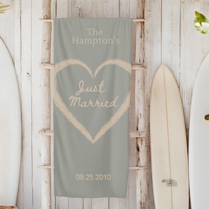 May include: A beach-themed wedding banner with the text "The Hampton's Just Married 09.25.2010" inside a heart shape. The banner is displayed on a wooden ladder, with surfboards and a woven basket nearby.