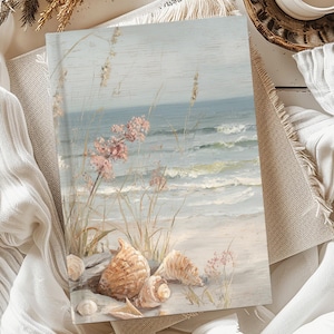 May include: A journal with a coastal beach scene on the cover, featuring seashells, pink flowers, and ocean waves. The journal is resting on a neutral-toned fabric, with a candle and dried plants in the background.