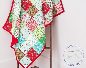 May include: A red and green patchwork quilt with a variety of Christmas-themed patterns. The quilt is folded and draped over a wooden ladder.