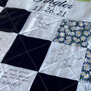 May include: A black and white quilt with a chequered pattern. The quilt has a date, "11.26.21", and the word "Ingler" written on it. There are several handwritten messages on the quilt, including "Love you! Aunt Celeste" and "We Love You! Bob, Ceny & Joseph Leclare".