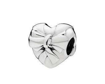 May include: A silver charm in the shape of a heart with a bow on the front. The charm has a polished finish and a hole for threading onto a bracelet or necklace. The bow is detailed with multiple layers.