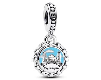 Puede incluir: Un charm de plata con un enganche en forma de corazón y un colgante redondo con la basílica de Santa Sofía en Estambul. El colgante tiene un fondo azul claro con la silueta del edificio y el texto "Hagia Sophia". El charm está decorado con detalles en forma de corazón.