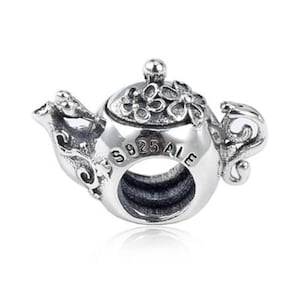 Könnte beinhalten: Ein silberner Charm in Form einer Teekanne. Der Charm hat florale Details auf dem Deckel und Ausguss, mit dem Text "S925 ALE" auf dem Körper. Der Charm ist für ein Armband oder eine Halskette konzipiert.