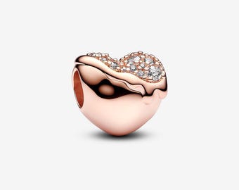 May include: A rose gold heart-shaped charm with a sparkling, textured top. The charm is adorned with numerous clear, round crystals, adding a touch of elegance. The charm has a smooth, polished finish and a small hole for attachment.