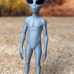 May include: A grey, humanoid alien figurine with a large, smooth, oval-shaped head and prominent, glossy black, almond-shaped eyes. The figure has a slender, muscular torso, thin arms and legs, and stands upright on a clear, circular plastic base.