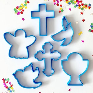 Puede incluir: Conjunto de seis cortadores de galletas de plástico azul con forma de paloma, cáliz, cruz, ángel y dos estilos diferentes de cruces.