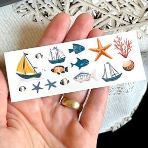 Peut inclure: Une feuille d'autocollants colorés sur le thème nautique. Les autocollants comprennent des voiliers, des poissons, des étoiles de mer, des coquillages et des coraux.