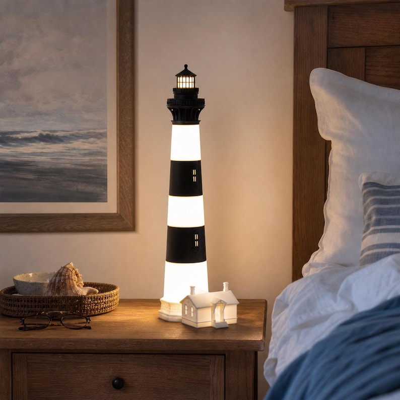 K&ouml;nnte beinhalten: Eine hohe, zylindrische Leuchtturm-Lampe mit abwechselnden horizontalen schwarzen und wei&szlig;en Streifen, einem schwarzen Laternenraum mit leuchtendem Licht und einem kleinen wei&szlig;en, hausf&ouml;rmigen Sockel, der ein warmes Licht ausstrahlt.