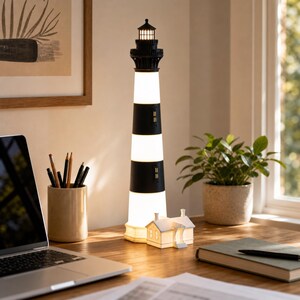 K&ouml;nnte beinhalten: Eine hohe, zylindrische Leuchtturm-Lampe mit abwechselnden horizontalen schwarzen und wei&szlig;en Streifen. Die Struktur ist mit einer schwarzen Laterne und einem leuchtenden Licht versehen. Am Fu&szlig; steht ein kleines, wei&szlig;es, detailliertes Haus.