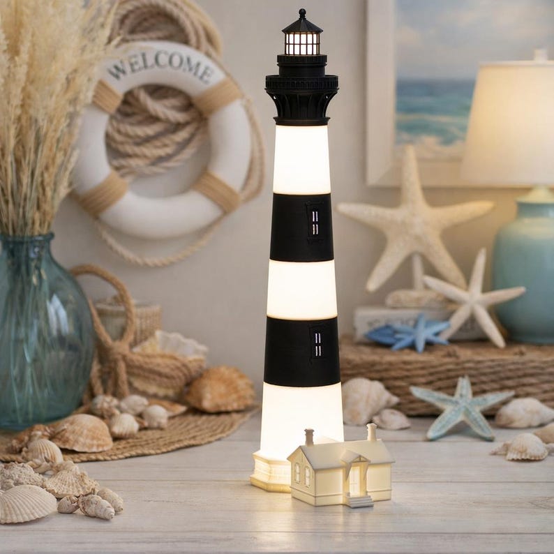 K&ouml;nnte beinhalten: Eine hohe, beleuchtete Leuchtturm-Lampe mit abwechselnden horizontalen schwarzen und wei&szlig;en Streifen, einem schwarzen Laternenraum an der Spitze und einem kleinen, wei&szlig; leuchtenden Haus an der Basis, das ein warmes Licht abgibt.