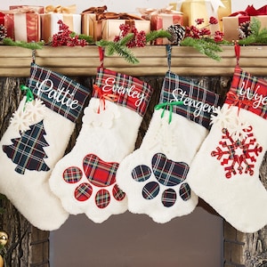 Puede incluir: Cuatro calcetines de Navidad blancos con ribete de tartán rojo y verde. Cada calcetín tiene un diseño bordado diferente: un árbol de Navidad, una huella de pata, un copo de nieve y otra huella de pata. Los calcetines están personalizados con los nombres "Pattie", "Everley", "Stenger" y "Wyeth".