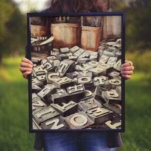 May include: A watercolor painting of a pile of vintage letterpress printing blocks, with the letters visible. The blocks are arranged in a random pattern, and some of the letters are partially obscured by others. The painting is framed in a black frame.