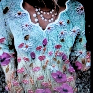May include: A light blue sweater with a V-neck and long sleeves, adorned with embroidered flowers in shades of white, pink, and purple. The floral design covers the front of the sweater, creating a garden-like appearance. A pearl necklace is visible.