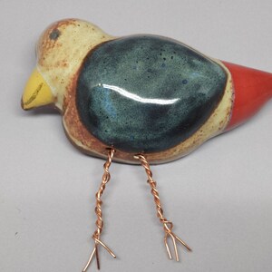 May include: A ceramic bird figurine with a blue, red, and brown glaze. The bird has copper wire legs.