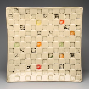 May include: A white ceramic square plate with a grid pattern and small squares of different colors, including red, orange, yellow, and green.
