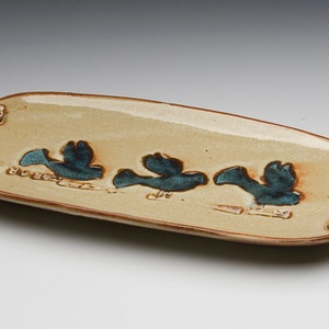 May include: A ceramic serving tray with brown rope handles and a beige glaze. The tray features three blue birds in flight.