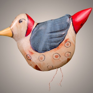 May include: A ceramic bird figurine with a red, yellow, and blue painted design. The bird has a long, thin beak and a small, round body. It has a blue wing and a red tail. The bird is decorated with white dots.