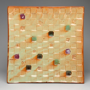 May include: A square ceramic serving dish with a light green glaze and a checkered pattern. The dish is decorated with small, colorful squares in shades of purple and green.