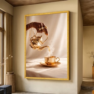 Könnte beinhalten: Gerahmter Kunstdruck, der eine goldene Teekanne zeigt, die Tee in eine passende Tasse und Untertasse gießt. Eine mit Schmuck verzierte Hand hält die Teekanne, Dampf steigt aus der Tasse auf. Das Kunstwerk hat einen goldenen Rahmen und hängt an einer beigefarbenen Wand.