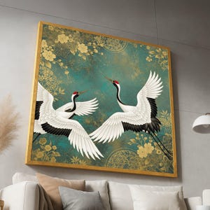 May include: A framed artwork featuring two Japanese cranes in flight. The birds have white feathers with black wingtips and red crowns, set against a teal background with gold floral accents. The frame is gold.