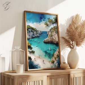 May include: A framed watercolor painting of a turquoise blue cove with white cliffs and a sailboat in the water. The cove is surrounded by lush green trees and there are people on the beach.