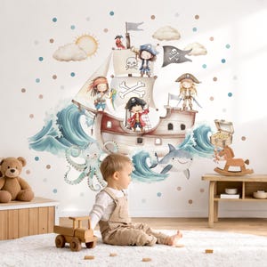 Op de afbeelding: Een muursticker-set met een aquarel piratenschip met drie cartoonpiraten, een vlag met doodskop, een haai, een octopus, een schatkist, zon, wolken en verspreide blauwe en bruine stippen op een witte achtergrond.