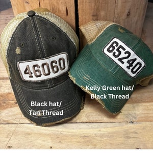 Puede incluir: Dos gorras de camionero con tejido desgastado y paneles de malla. La gorra negra tiene hilo de color canela y el número 46060 en la parte delantera. La gorra verde kelly tiene hilo negro y el número 65240 en la parte delantera.