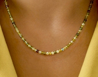 May include: A delicate necklace composed of small, faceted, multi-colored gemstone beads in shades of olive green, yellow, and clear white. The beads are strung together in a continuous strand that rests against the neck, featuring a subtle sparkle.