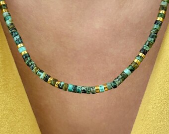 May include: A beaded necklace featuring small, cylindrical turquoise-colored stone beads with mottled green and blue patterns, interspersed with polished gold-tone metal spacer beads arranged in a repeating pattern around the entire length.