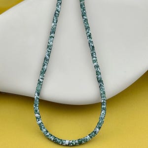 May include: A single strand of small, disc-shaped beads featuring a mottled pattern of deep forest green and white. The beads are uniform in size and shape, strung together to form a continuous loop, showcasing a marbled texture throughout the strand.
