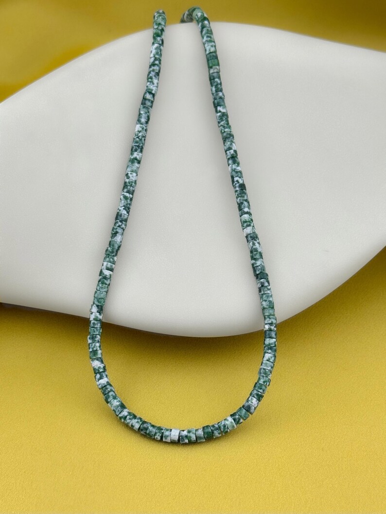 May include: A single strand of small, disc-shaped beads featuring a mottled pattern of deep forest green and white. The beads are uniform in size and shape, strung together to form a continuous loop, showcasing a marbled texture throughout the strand.
