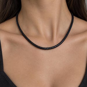May include: A necklace composed of small, uniform, cylindrical black beads strung together in a single strand. The beads have a smooth, glossy finish and are arranged closely to form a continuous, circular chain that rests around the neck.