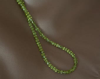 May include: A single strand of small, faceted, translucent lime green beads arranged in a simple loop. The beads are uniform in size and shape, reflecting light across their cut surfaces to create a subtle sparkle along the length of the necklace.